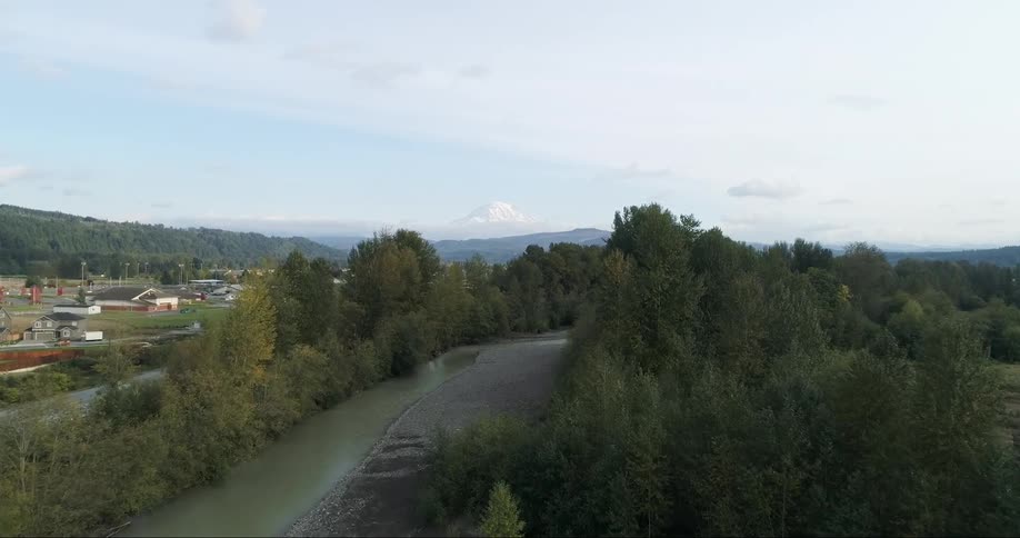 A river surrounded by trees with houses trees and the sky in the background