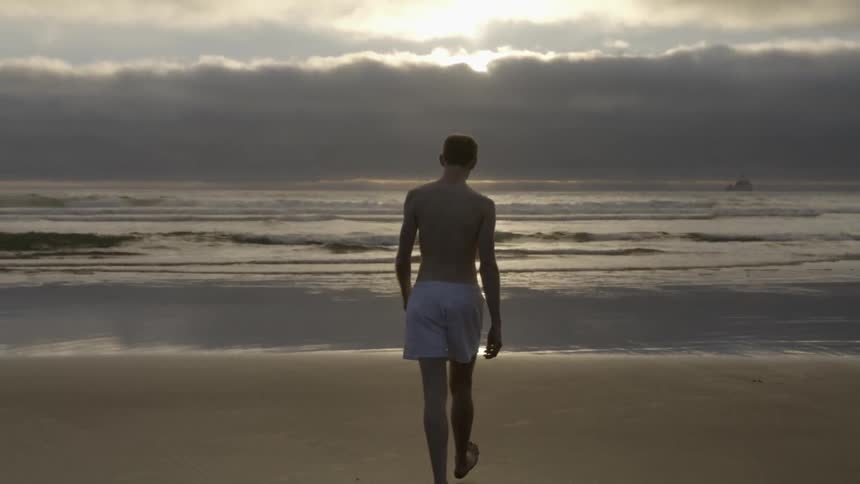 A man slowly walks over to the water at the beach