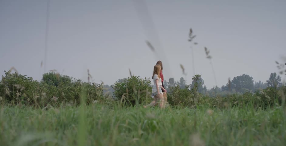 A pair of young women walk through a field of grass while carrying tin pails