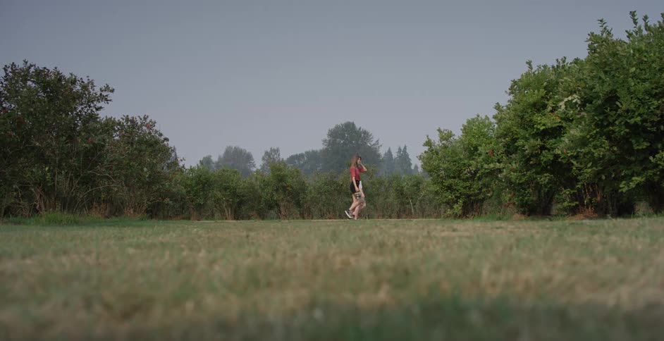 Woman with a red blouse and black shorts and blonde woman with a white shirt and blue shorts carries buckets walk in the cherry orchard