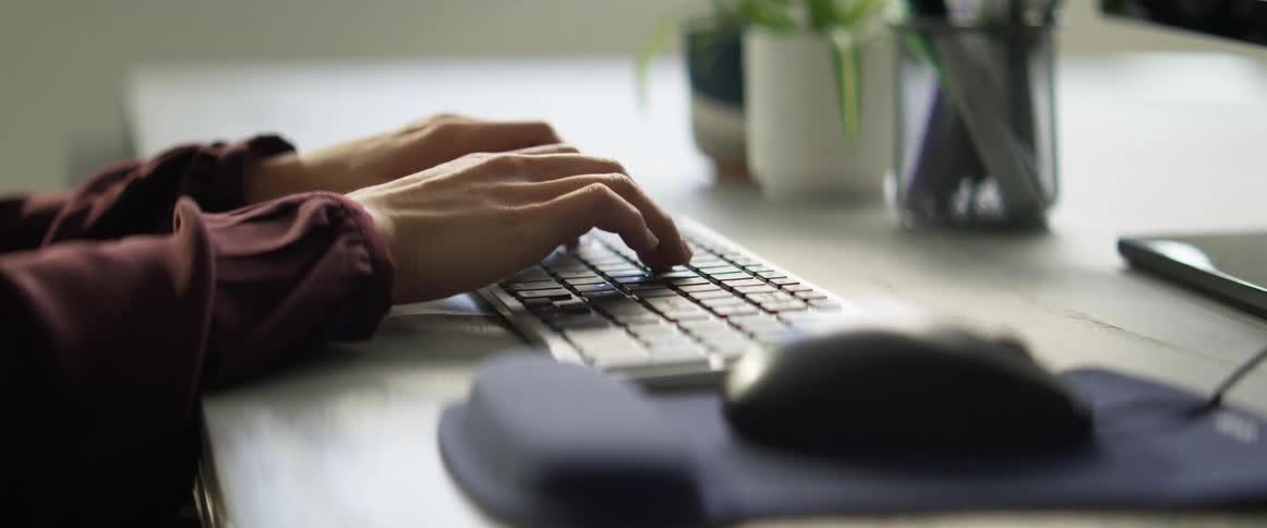 Woman with a brown shirt sitting down at a desk uses a computer mouse and types on a keyboard