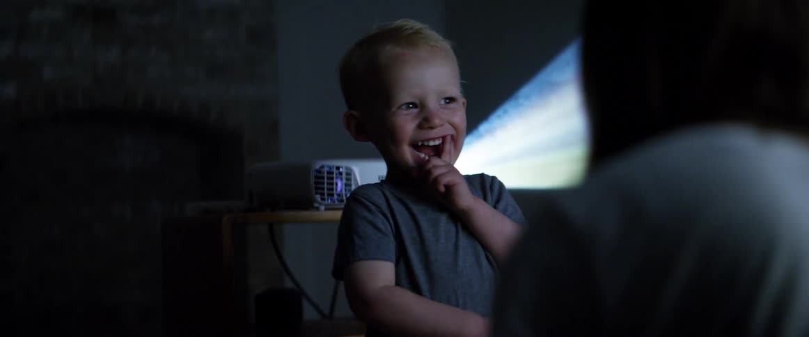 A woman tickles her son as a projector plays in their home