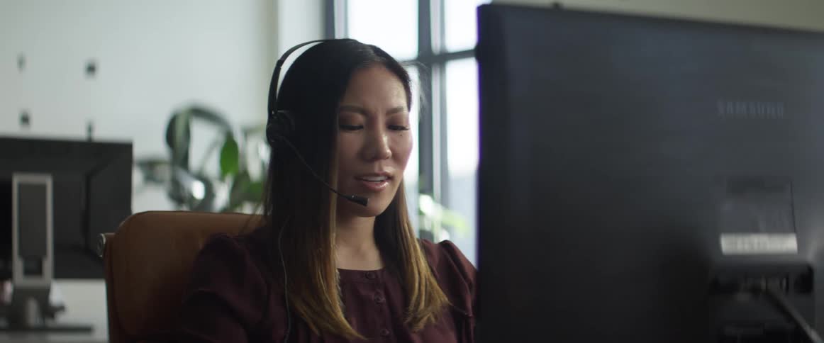 Woman talks in a headset in the office in front of a computer screen