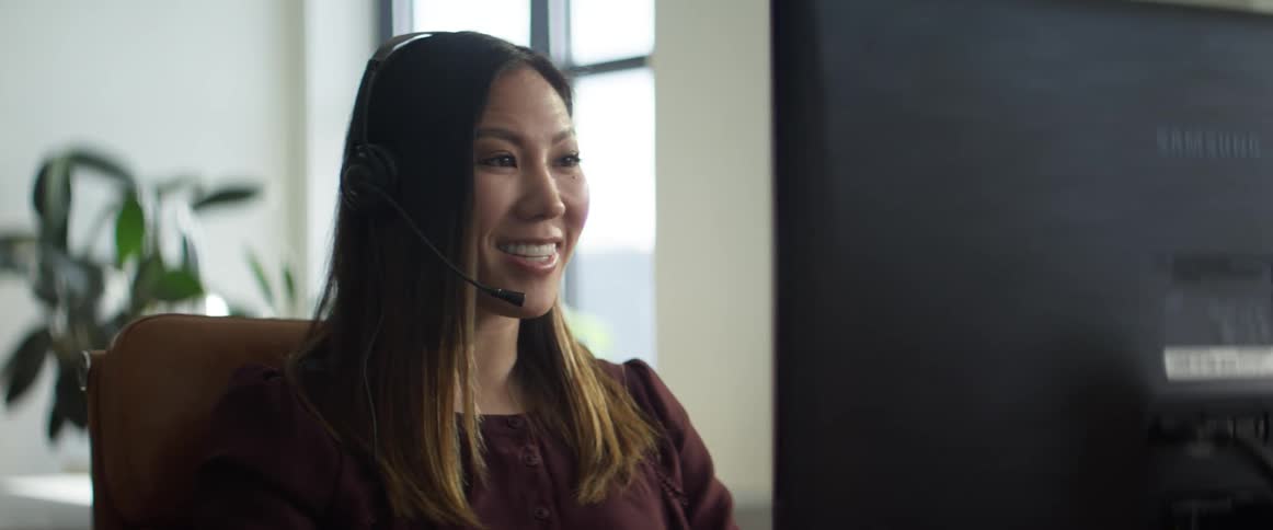A woman in an office talks on the phone while using the computer