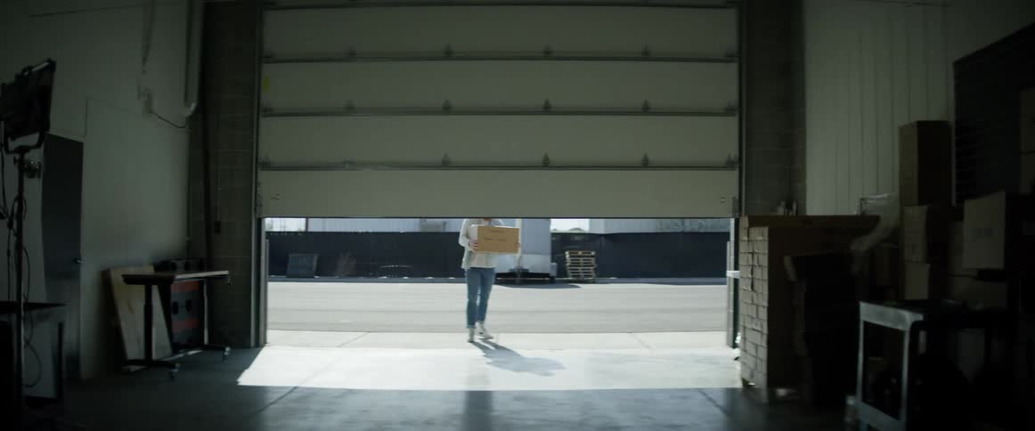 Two men carry boxes in a storage unit as a sliding door raises up