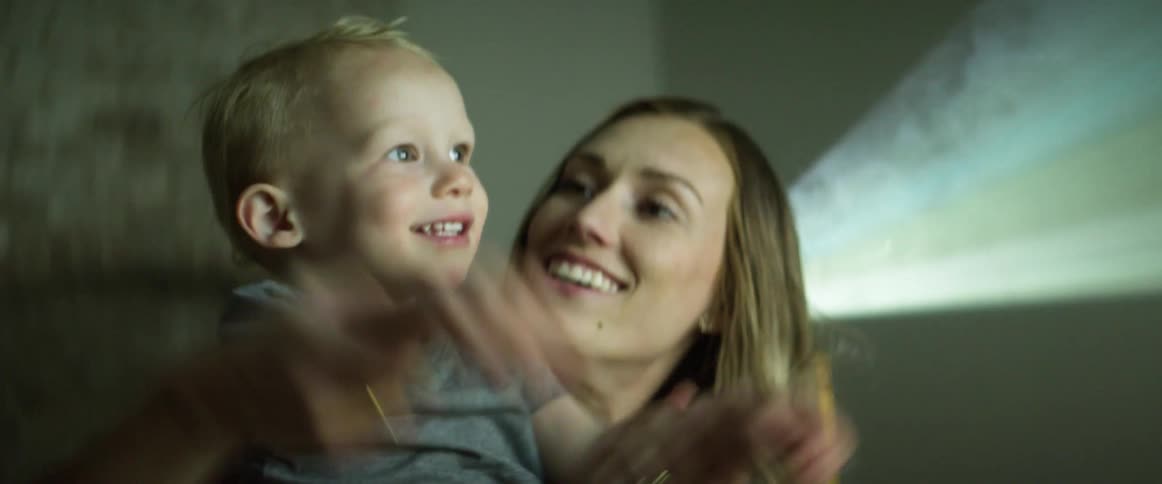 A woman and a boy watching a projection with a projector behind them