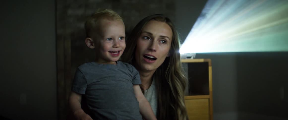 A woman tickling a boy while watching a projection with a projector behind them