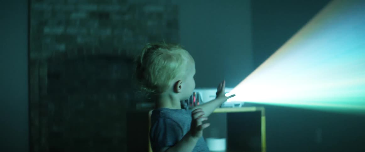 A man watches his young toddler son look at a projection screen