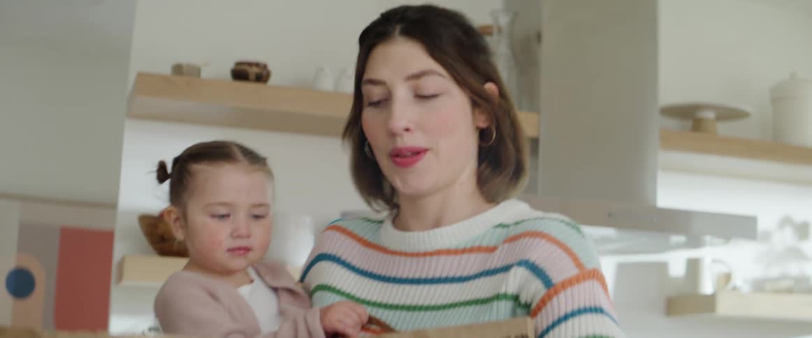 Woman carries a girl and groceries in her hands into the kitchen