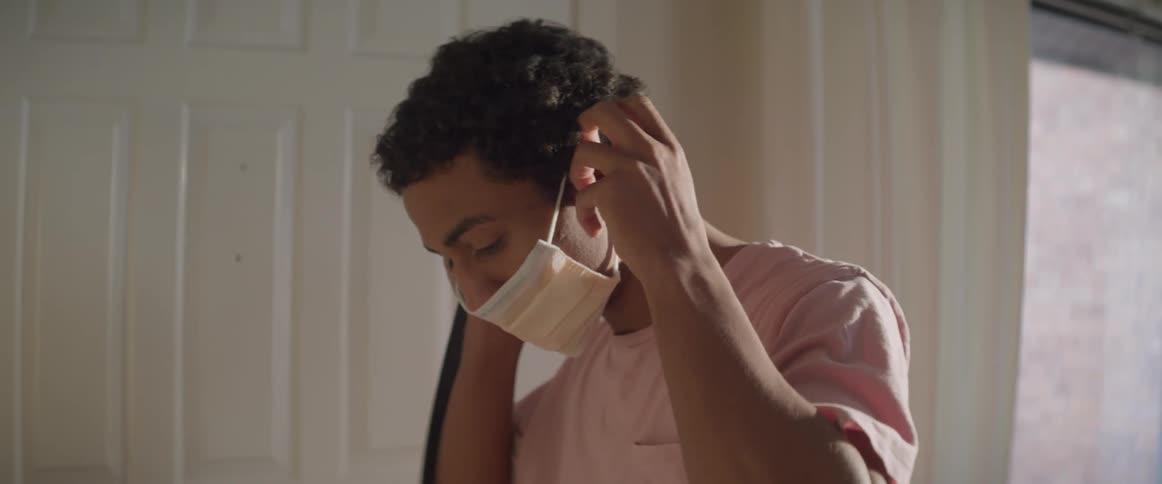 A young man puts on a medical mask before turning to open a door