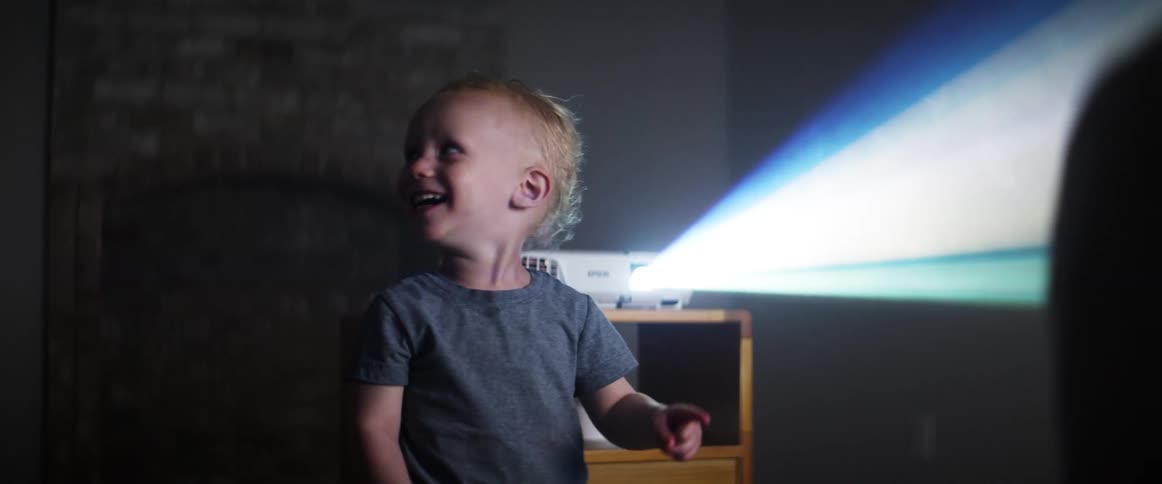Boy smiles and laughs looking at a movie projected in a dimly lit room at home