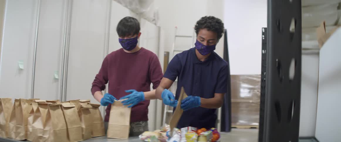 Two teenage boys put food in brown lunch bags