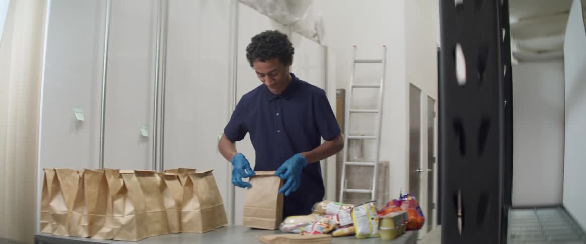Young man prepares brown paper bag lunches on countertop