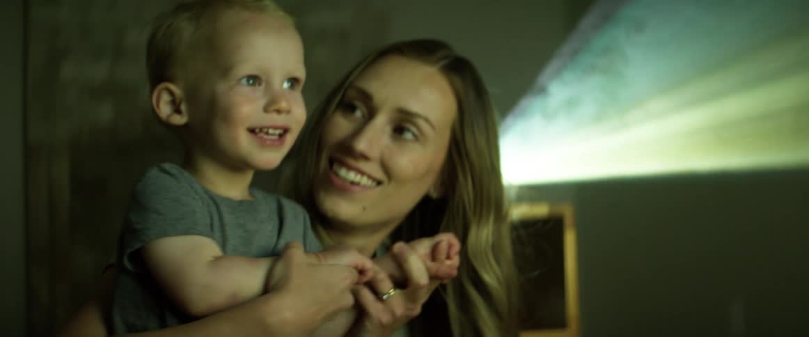 A woman and a boy looking and smiling at a projection with a projector behind them