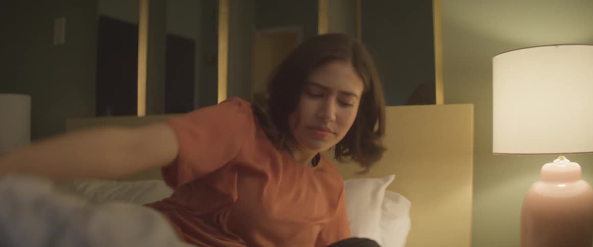 Woman with an orange shirt wakes up and turns on the lamp to get up in the bedroom