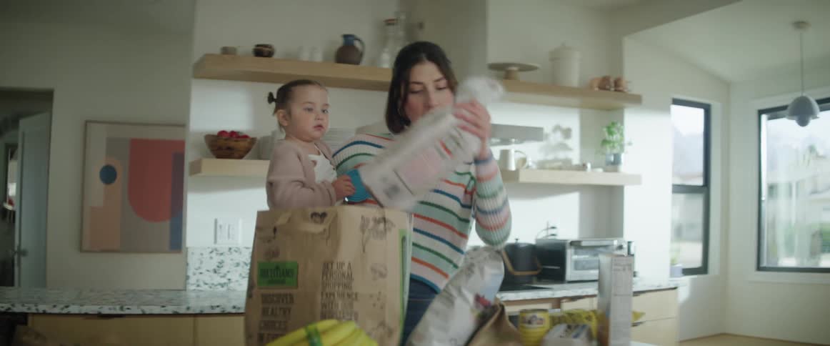 Mother holding child while unpacking groceries in the kitchen
