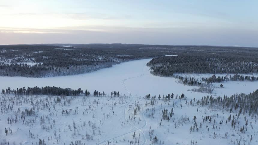 Aerial view of a frozen river surrounded by snow covered pine forests