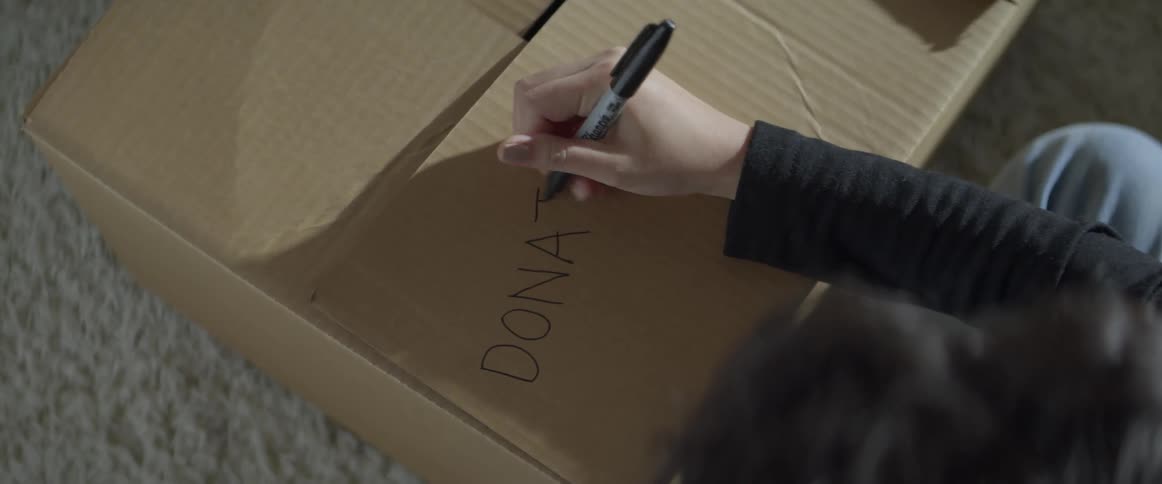 A woman writes on a cardboard box for items to donate