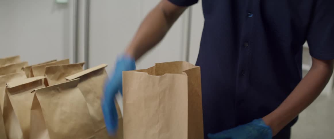 A woman wearing blue gloves is preparing sack lunches