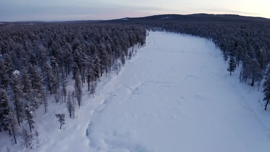 An aerial view of a large snowy clearing surrounded by a dense forest