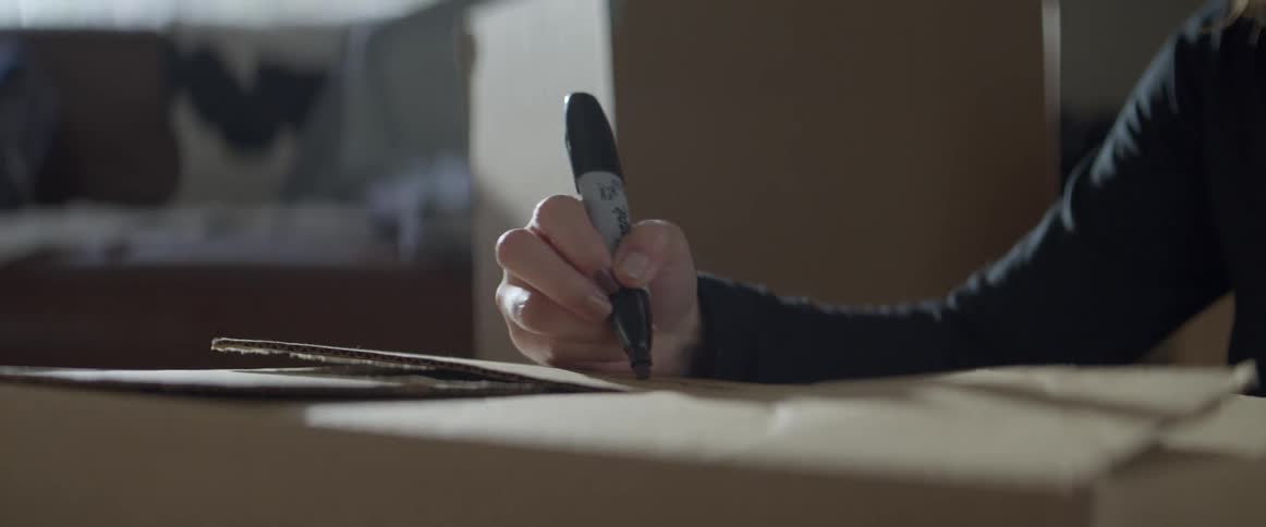 A person uses a sharpie marker to right on a moving box