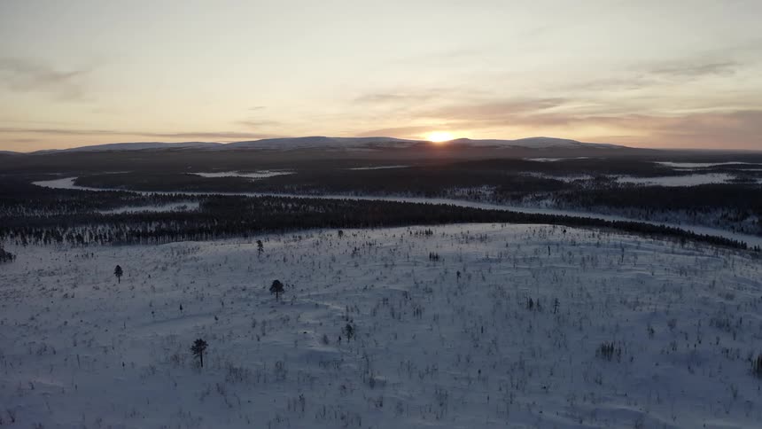 The sun rises over a barren arctic wilderness covered in snow and trees