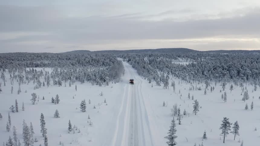 Aerial view of a snow plow driving down a snowy road next to a forest