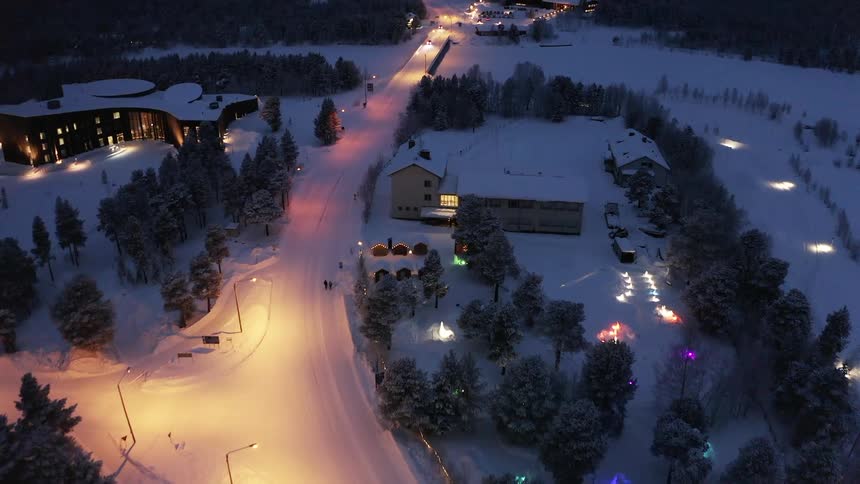 A snow covered road through a small town in a wintery landscape at night