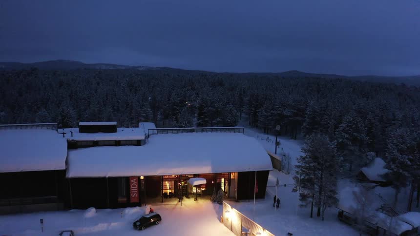 Aerial view of a person walking out of a restaurant surrounded by trees on a snowy evening