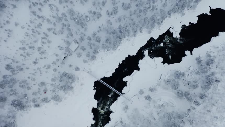 Aerial top down view of a river near a snow covered pine forest at winter