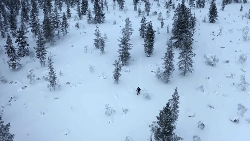 A man carefully hikes through a forest covered in a thick blanket of snow