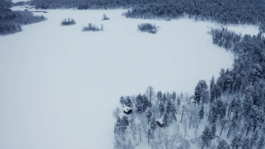 Houses at the shoreline of a frozen lake in a snow covered pine tree forest in winter