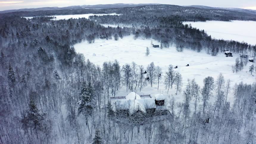 Aerial view of a group of snowmobiles arriving at a rural house in the forest at winter