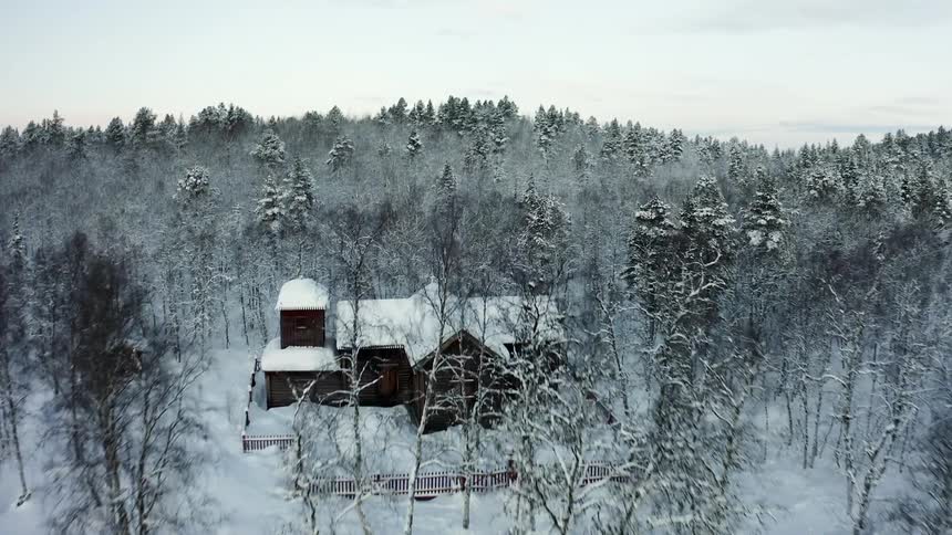 Aerial view of a house in a rural area covered in snow in front of a forest