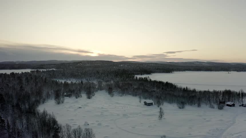 A farm stead is nestled against a snowy forest