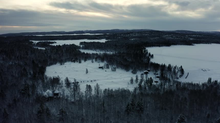 Aerial view of people walking through the snow in an area surrounded by dense forest