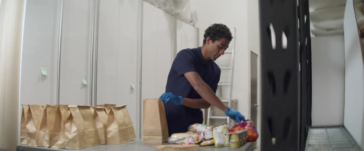 Man wearing latex gloves puts groceries in paper bags in a warehouse