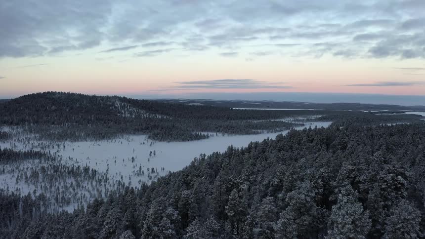 Aerial view revealing a valley between forest covered mountains in the sunset at winter