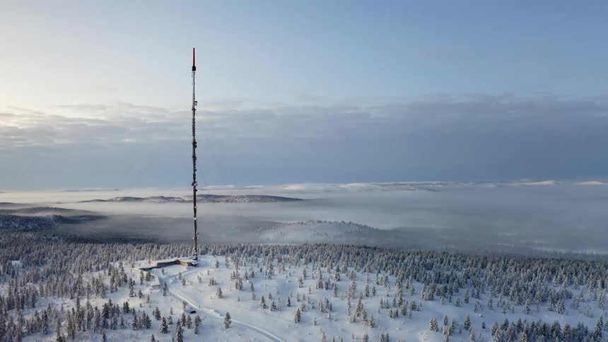 A tall radio tower on a hill overlooking a snow covered valley shrouded in fog