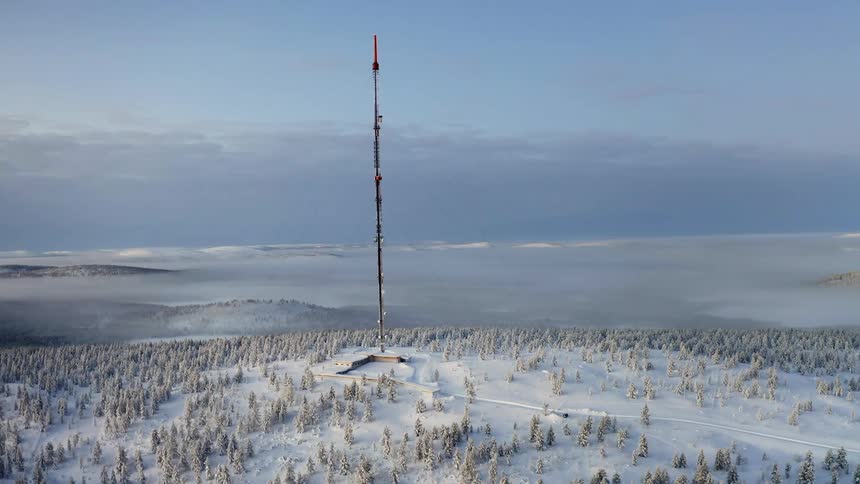 A building with an antenna surrounded by trees covered in snow with the sky in the background