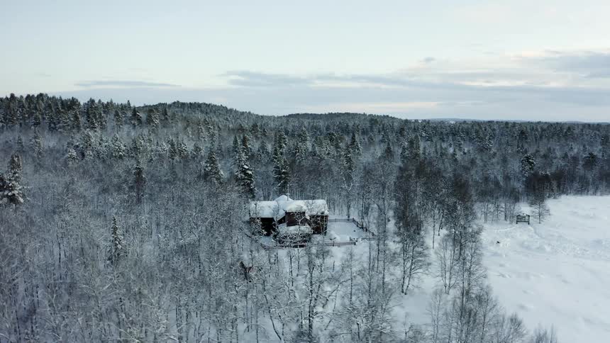 A lonely house sits covered in snow just inside the forest in winter
