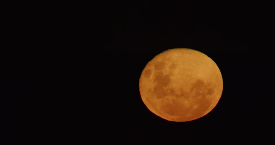 Yellow full moon rising in the pitch black sky at night