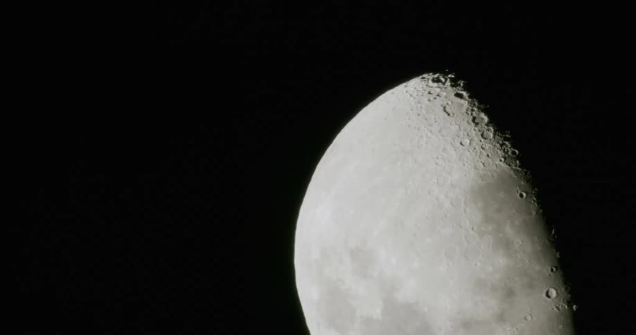 A partial moon is illuminated on a dark night