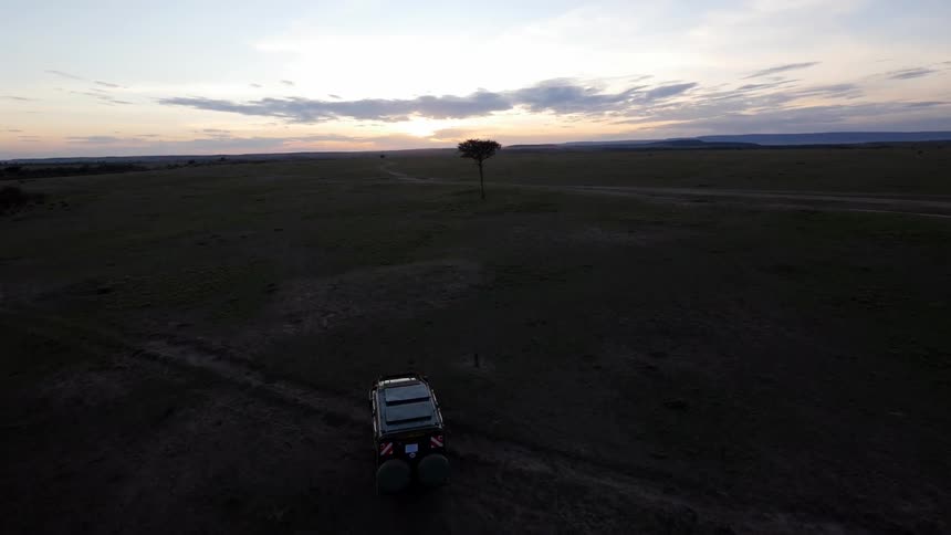 A vehicle is driving across a field at sunset