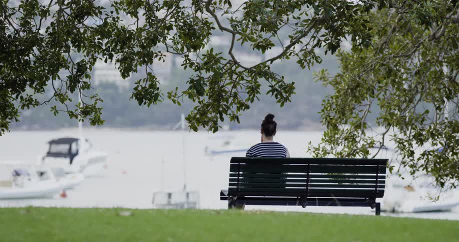 Woman sitting on a bench under a tree at the seaside