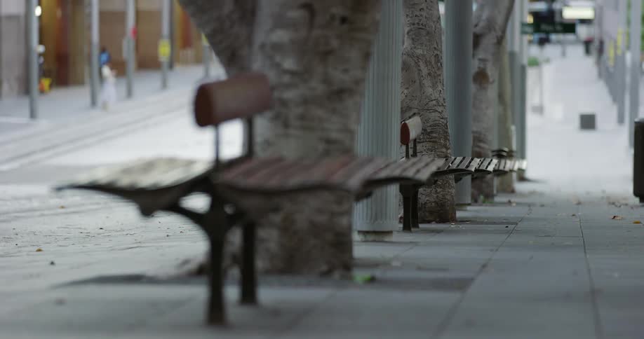 Bench sits on the sidewalk as pedestrians walk nearby