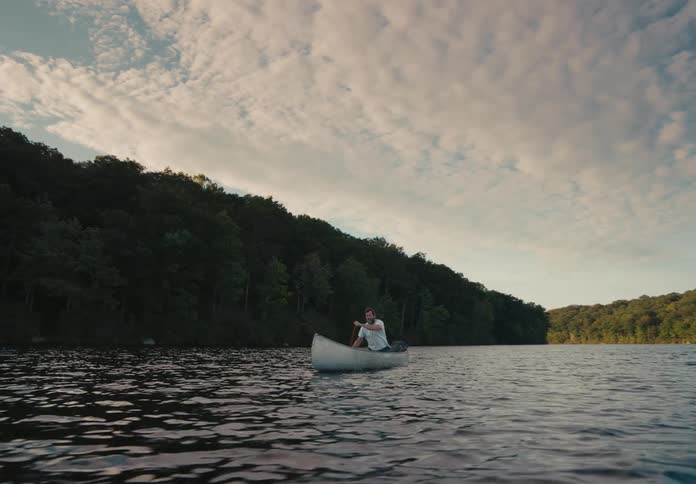 A man in a rowboat on a lake paddling with trees and the sky in the background