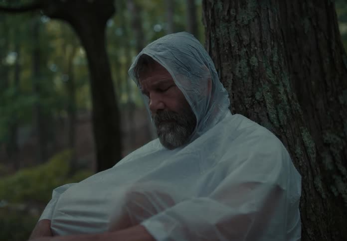 A man in a raincoat sits against a tree sleeping