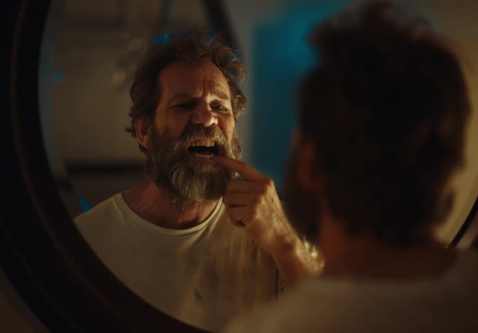 A bearded man checks his teeth in a mirror