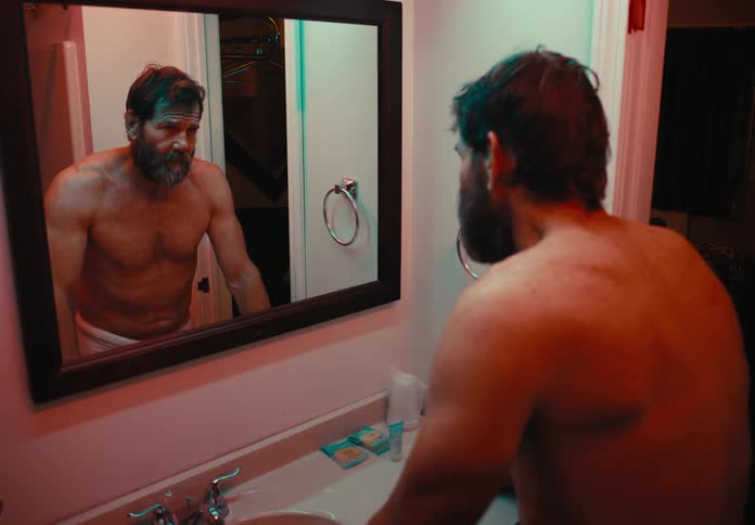 A man stands in front of a bathroom sink and mirror contemplating something